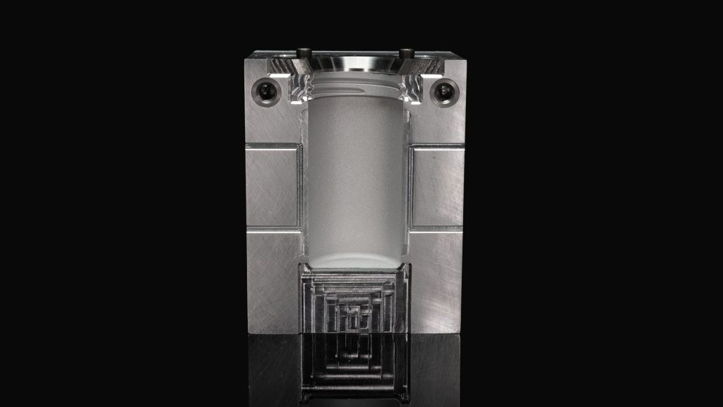 Half of a hybrid manufactured, silver-metallic mold sits on a reflective, black surface, revealing the internal cavity. Hybrid manufacturing is an excellent option for mitigating corrosion and abrasion in plastics tooling.