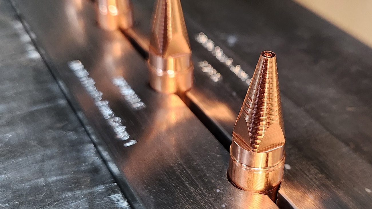 cnc manufactured copper meltio replacement nozzles, lined up in a row in a vice.