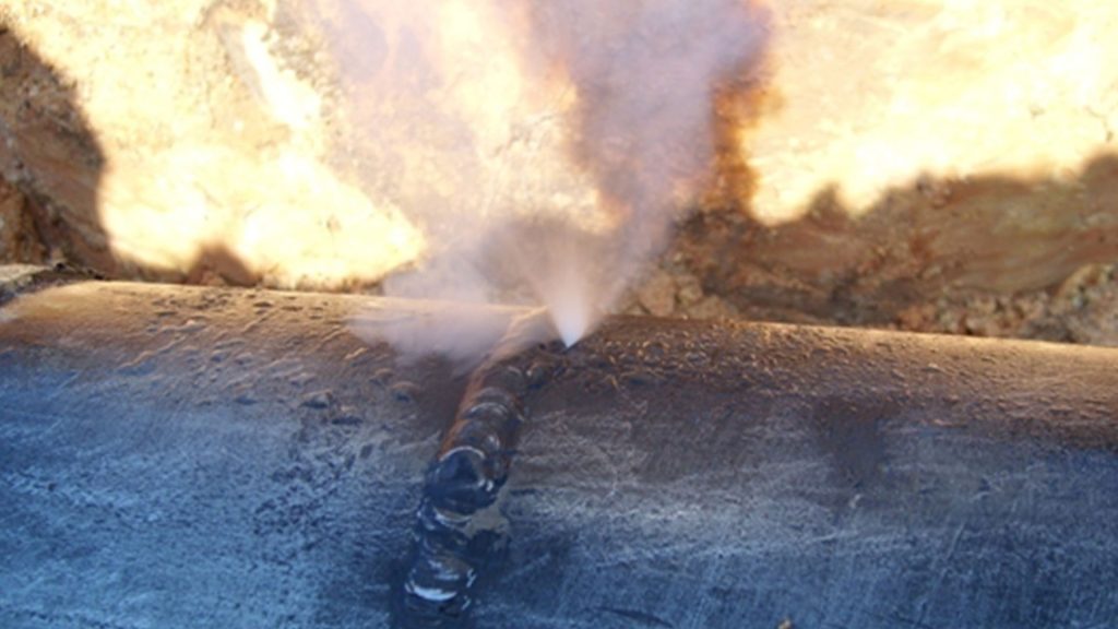 Steam issues from a crack in a metal pipe as a result of stress corrosion cracking.